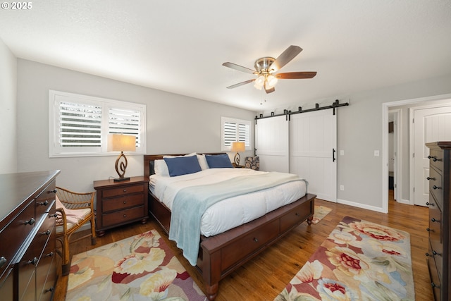 bedroom featuring ceiling fan, a barn door, wood finished floors, and baseboards