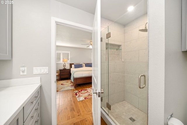 ensuite bathroom featuring a ceiling fan, a stall shower, vanity, ensuite bath, and wood finished floors