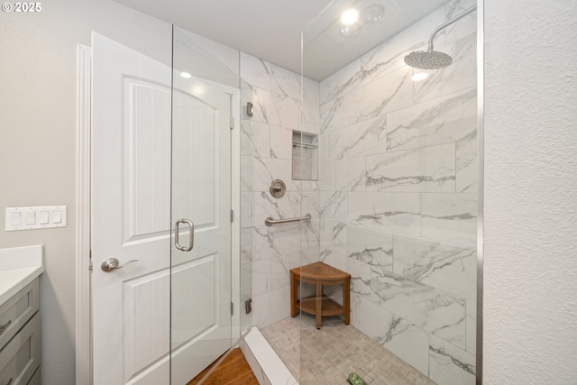 bathroom with a textured wall, a shower stall, and vanity