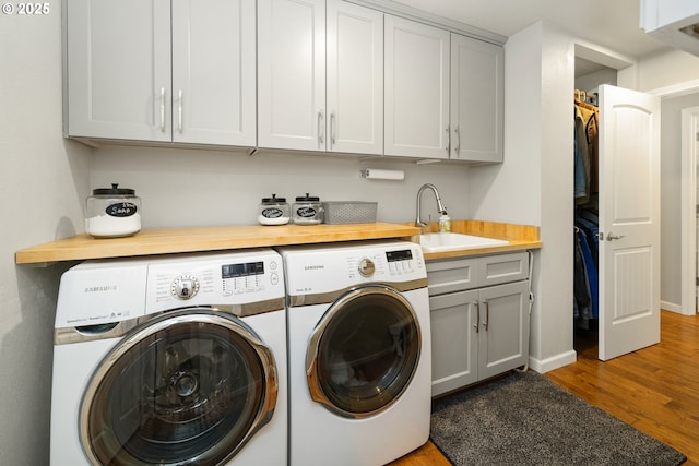 clothes washing area with wood finished floors, a sink, baseboards, cabinet space, and washer and clothes dryer