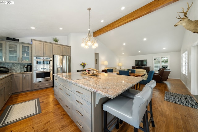 kitchen featuring a kitchen island, glass insert cabinets, vaulted ceiling with beams, stainless steel appliances, and light wood-type flooring