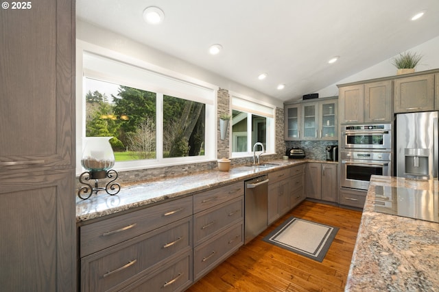 kitchen featuring stainless steel appliances, decorative backsplash, glass insert cabinets, vaulted ceiling, and a sink