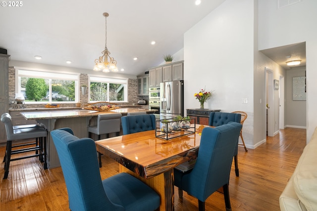 dining area with baseboards, light wood-type flooring, high vaulted ceiling, a notable chandelier, and recessed lighting