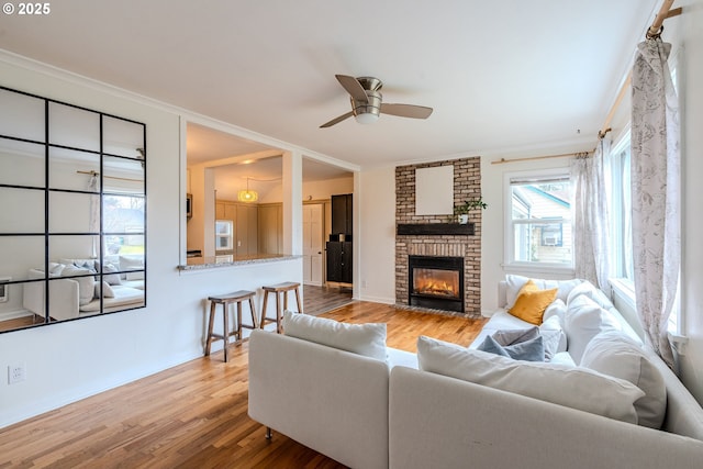 living room with ceiling fan, ornamental molding, a brick fireplace, and light hardwood / wood-style flooring