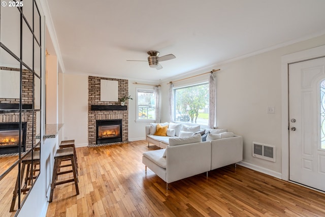 living room with ornamental molding, ceiling fan, a fireplace, and light hardwood / wood-style floors