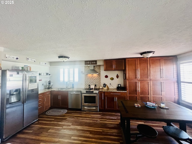 kitchen with decorative backsplash, dark wood-style floors, appliances with stainless steel finishes, wall chimney range hood, and a sink