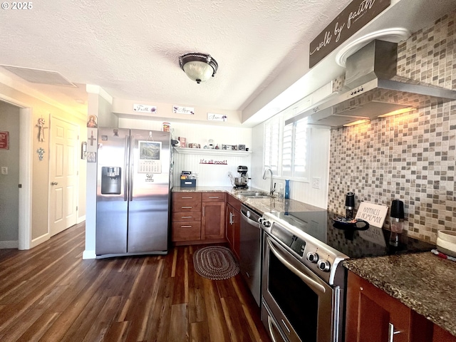 kitchen featuring decorative backsplash, wall chimney exhaust hood, dark wood-style flooring, stainless steel appliances, and a sink