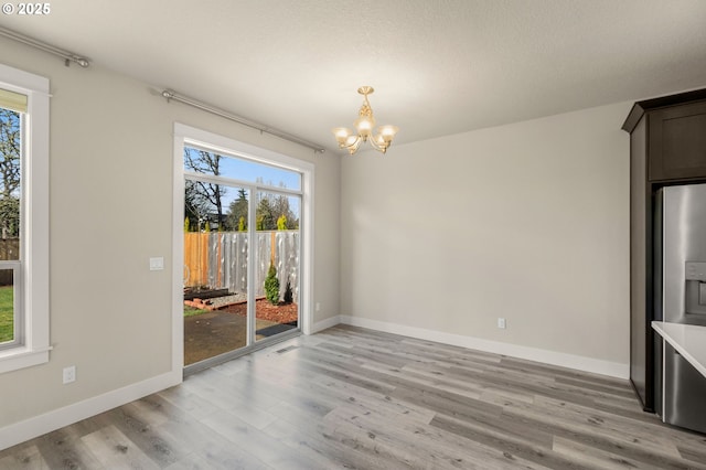 unfurnished dining area with baseboards, light wood finished floors, visible vents, and a notable chandelier