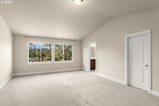 unfurnished room featuring light carpet, a textured ceiling, lofted ceiling, and baseboards