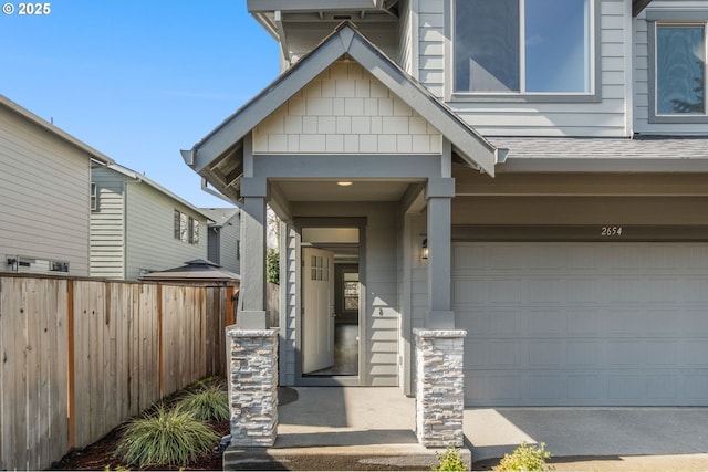 view of exterior entry featuring a garage, a shingled roof, and fence