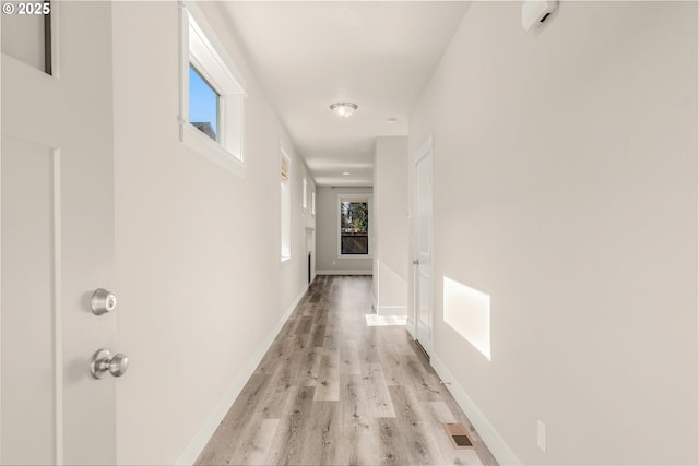 corridor with baseboards, visible vents, and light wood finished floors