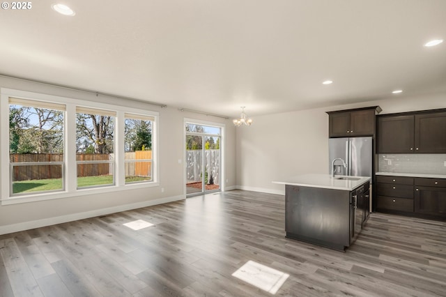 kitchen with dark brown cabinetry, a sink, light countertops, stainless steel refrigerator with ice dispenser, and backsplash