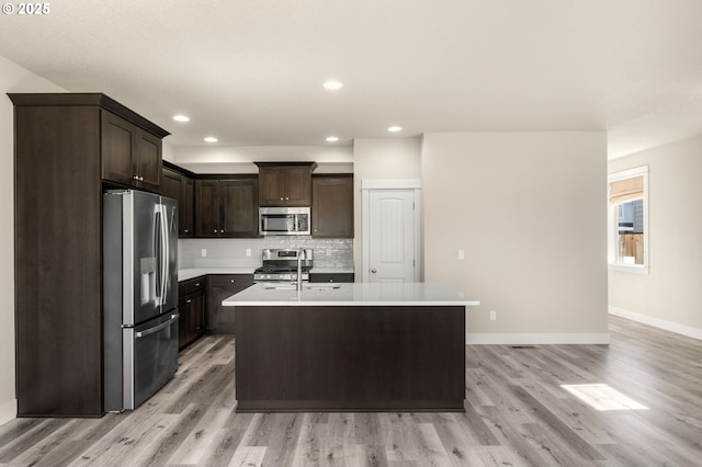 kitchen featuring stainless steel appliances, dark brown cabinets, light countertops, light wood-type flooring, and backsplash