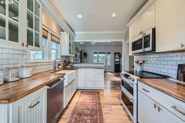 kitchen with crown molding, wooden counters, appliances with stainless steel finishes, plenty of natural light, and a peninsula