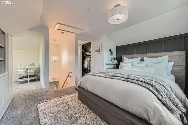 bedroom with vaulted ceiling, a spacious closet, a decorative wall, and carpet flooring