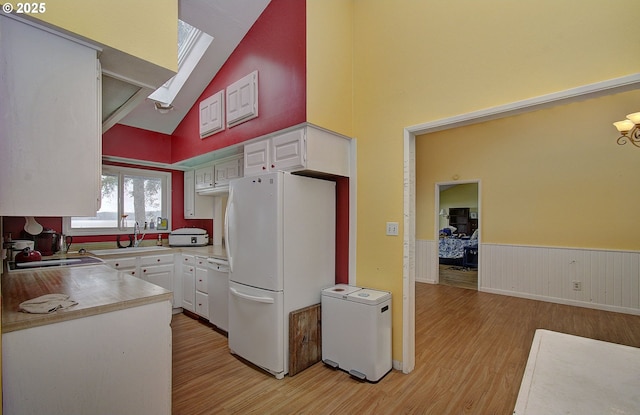 kitchen featuring white appliances, a skylight, white cabinets, and light wood-type flooring