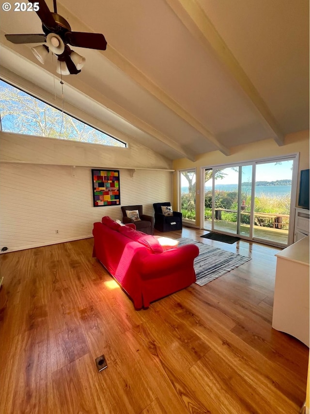 living area with a ceiling fan, wood finished floors, and vaulted ceiling with beams