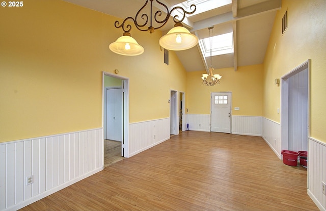 empty room with wood-type flooring, high vaulted ceiling, a chandelier, and a skylight