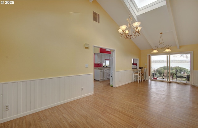 unfurnished living room featuring vaulted ceiling with skylight, a chandelier, and light hardwood / wood-style flooring