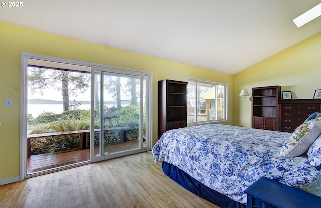 bedroom featuring a water view, vaulted ceiling with skylight, access to exterior, and wood finished floors