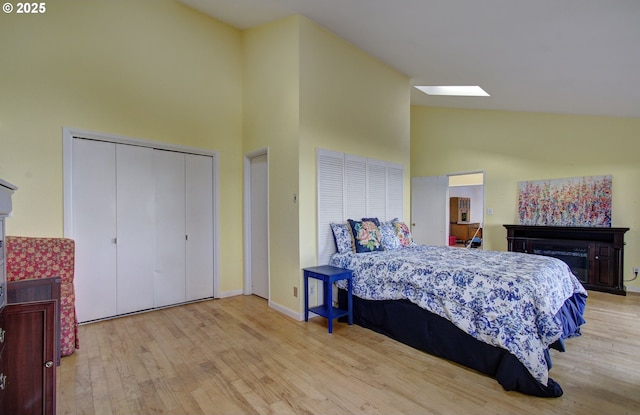 bedroom featuring baseboards, high vaulted ceiling, wood finished floors, and a fireplace