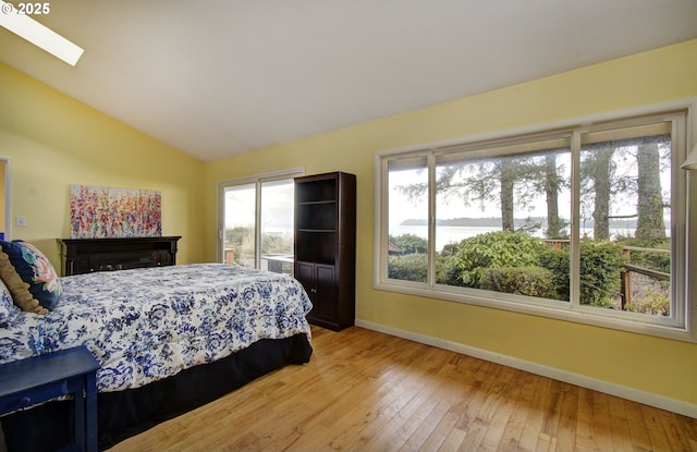 bedroom featuring vaulted ceiling with skylight, baseboards, and light wood-type flooring