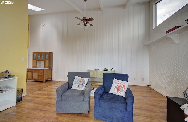 sitting room featuring beamed ceiling, ceiling fan, a skylight, and light wood-type flooring