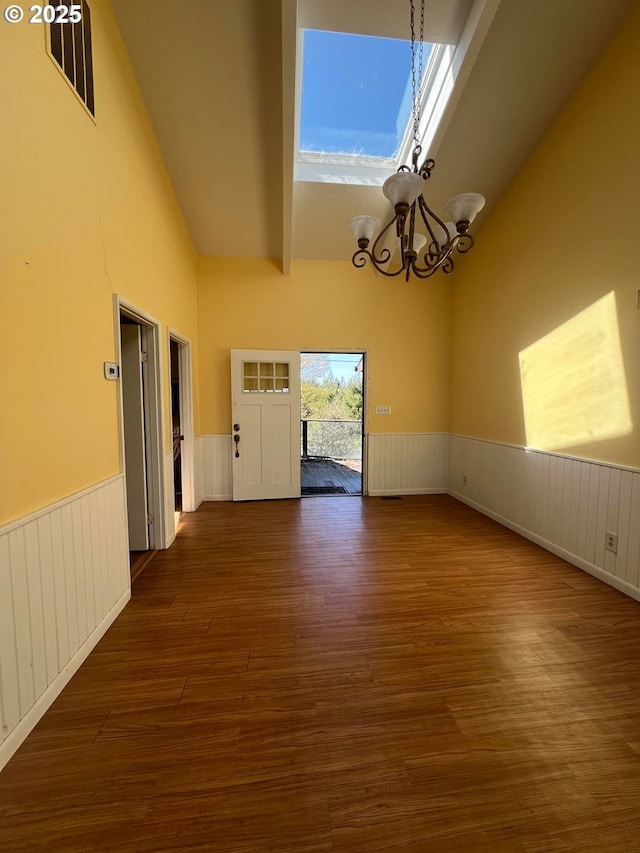 interior space with a chandelier, high vaulted ceiling, wainscoting, and dark wood-style flooring