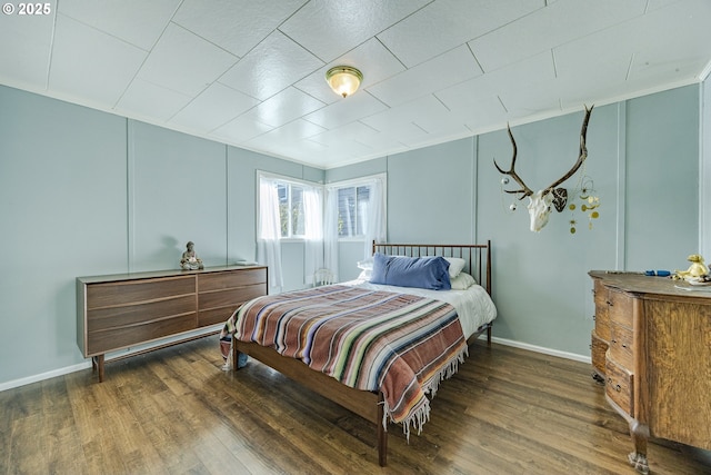 bedroom with baseboards, a decorative wall, and wood finished floors