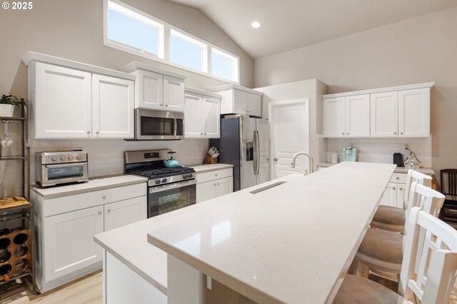 kitchen with appliances with stainless steel finishes, a sink, a breakfast bar area, a toaster, and backsplash