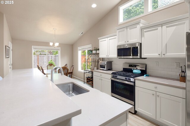 kitchen with appliances with stainless steel finishes, a sink, white cabinetry, lofted ceiling, and tasteful backsplash