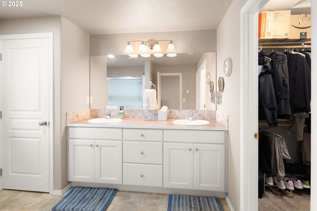 bathroom with double vanity, a sink, baseboards, and a spacious closet