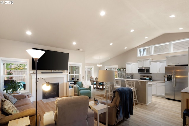living room with visible vents, lofted ceiling, recessed lighting, a fireplace with flush hearth, and light wood-style flooring