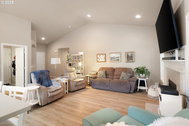living room featuring a fireplace, vaulted ceiling, recessed lighting, and light wood-style flooring