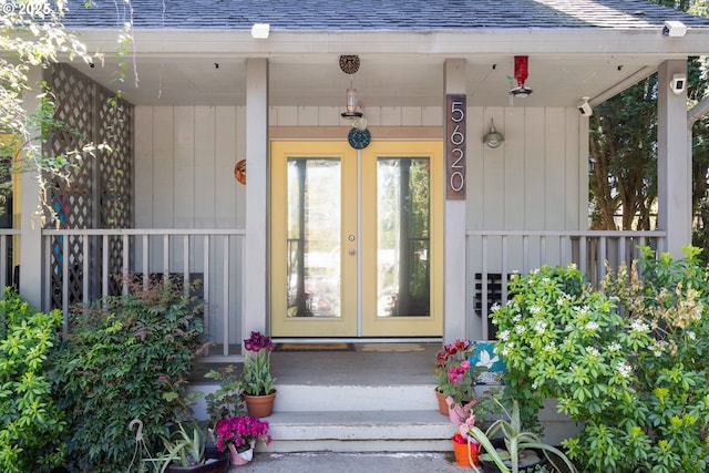 property entrance with french doors, a shingled roof, covered porch, and fence