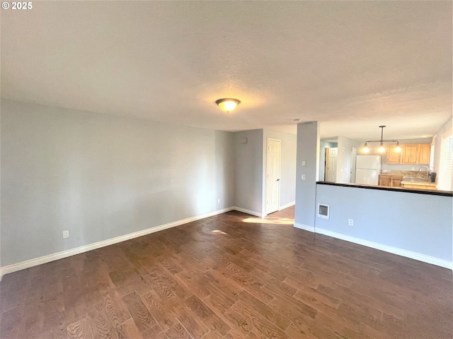 unfurnished living room featuring baseboards, dark wood-style flooring, a textured ceiling, and visible vents