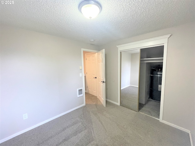 unfurnished bedroom featuring a textured ceiling, a closet, water heater, carpet flooring, and visible vents