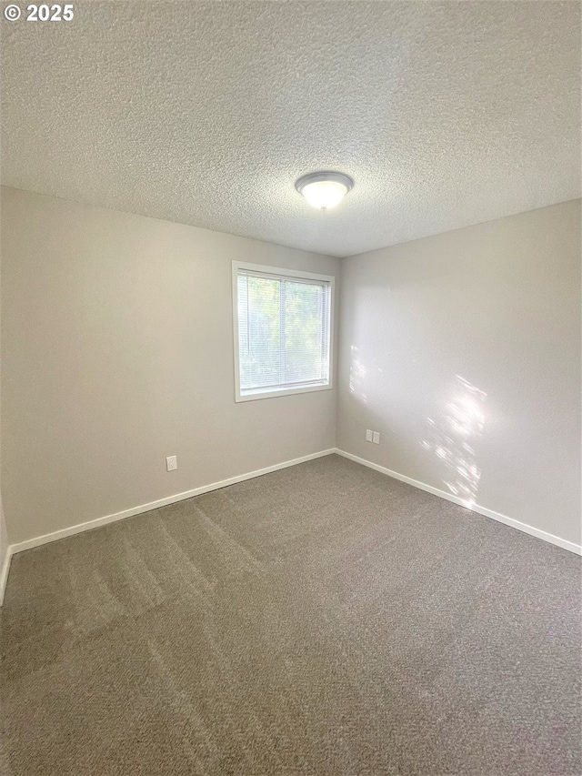 empty room featuring dark carpet, a textured ceiling, and baseboards