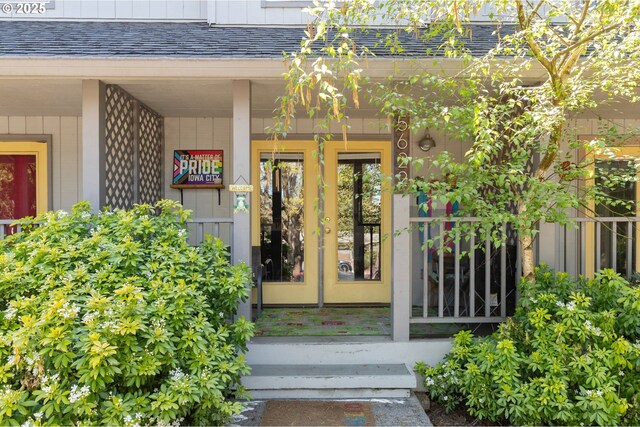 doorway to property featuring french doors, roof with shingles, and a porch