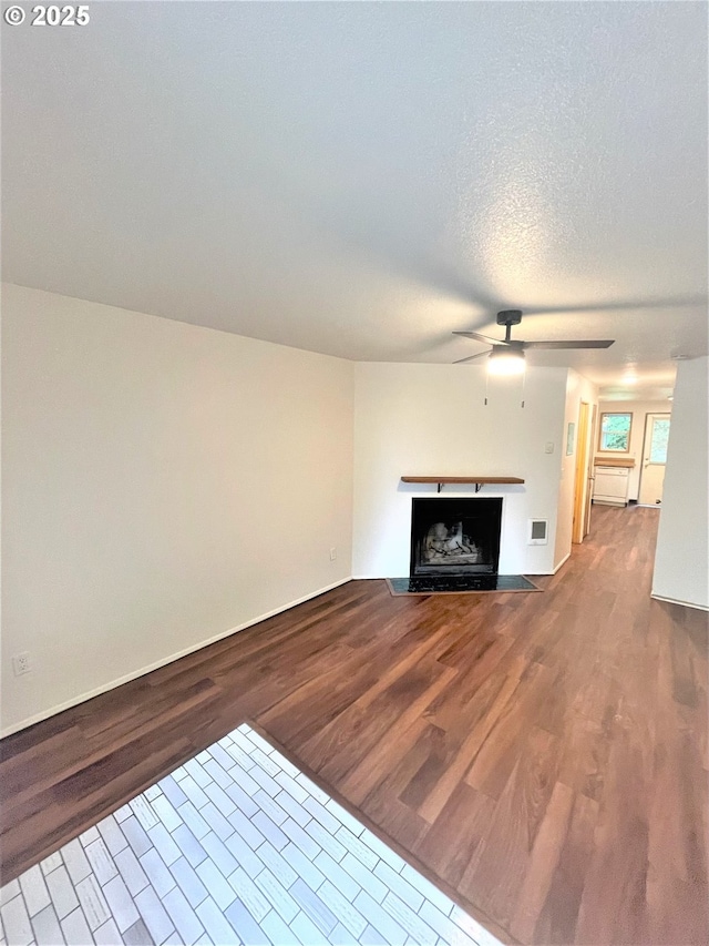 unfurnished living room with wood finished floors, visible vents, a ceiling fan, baseboards, and a fireplace