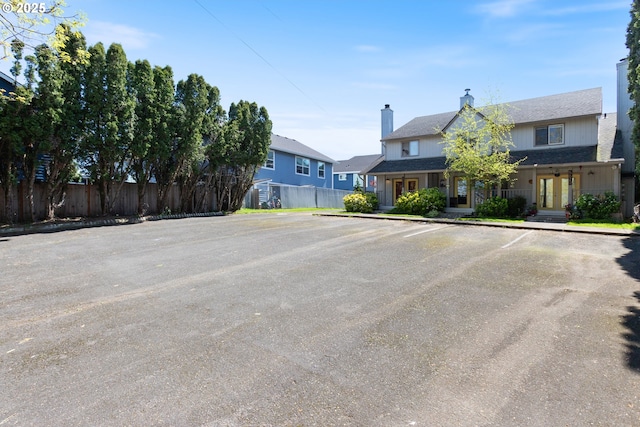 view of front of home featuring uncovered parking, fence, a chimney, and french doors
