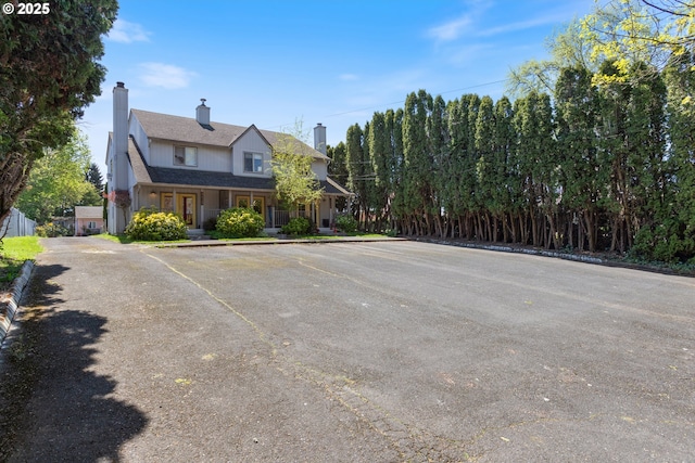 view of side of home featuring uncovered parking, a porch, a chimney, and a shingled roof