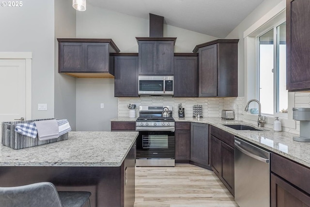 kitchen featuring stainless steel appliances, a sink, lofted ceiling, decorative backsplash, and dark brown cabinetry