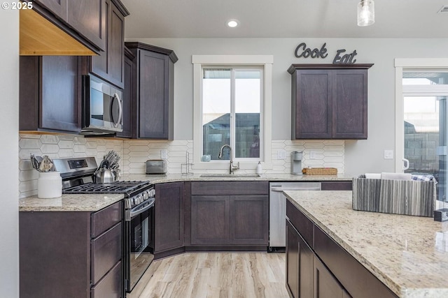 kitchen with stainless steel appliances, a sink, light stone countertops, dark brown cabinets, and recessed lighting