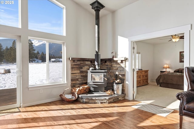 living room with ceiling fan, a towering ceiling, a wood stove, and light hardwood / wood-style floors