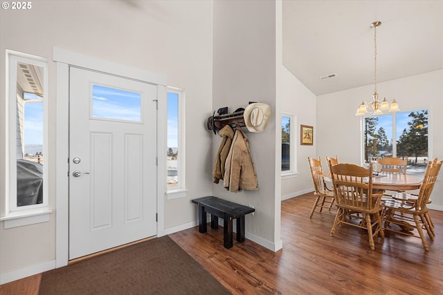 foyer entrance featuring a healthy amount of sunlight, vaulted ceiling, dark hardwood / wood-style flooring, and a chandelier