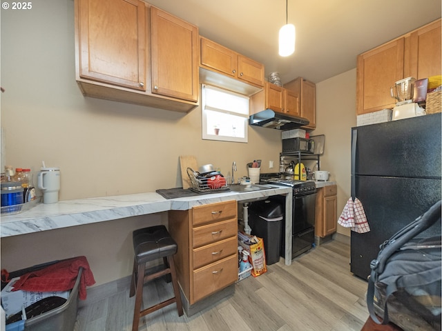 kitchen with black fridge, gas range, hanging light fixtures, a kitchen breakfast bar, and light hardwood / wood-style floors