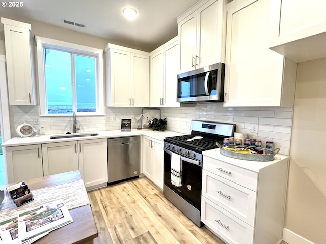 kitchen featuring light hardwood / wood-style floors, stainless steel appliances, backsplash, white cabinets, and sink