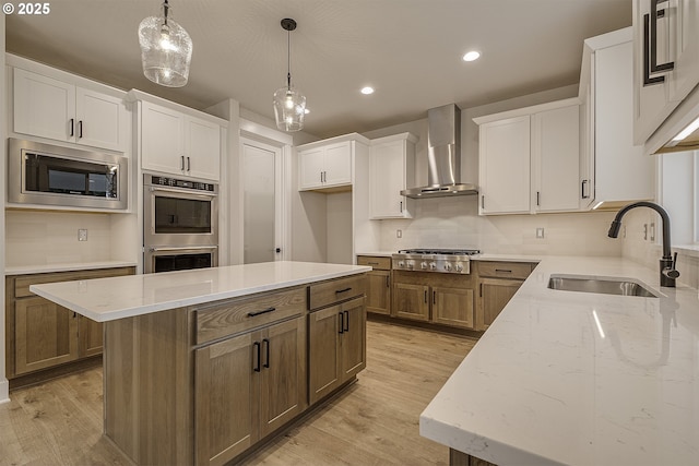 kitchen with light stone counters, a sink, stainless steel appliances, wall chimney range hood, and white cabinets