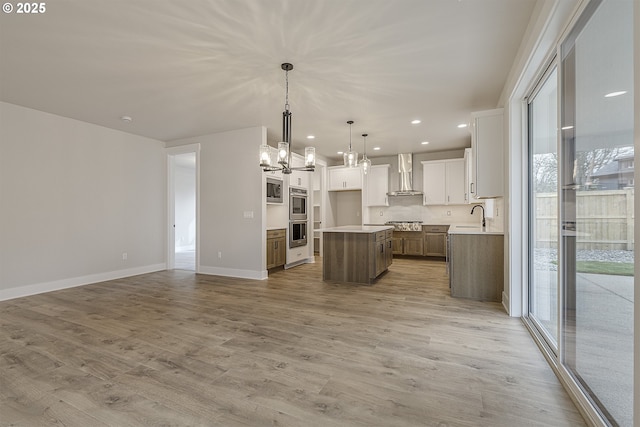 kitchen with open floor plan, light wood-type flooring, a chandelier, double oven, and wall chimney range hood